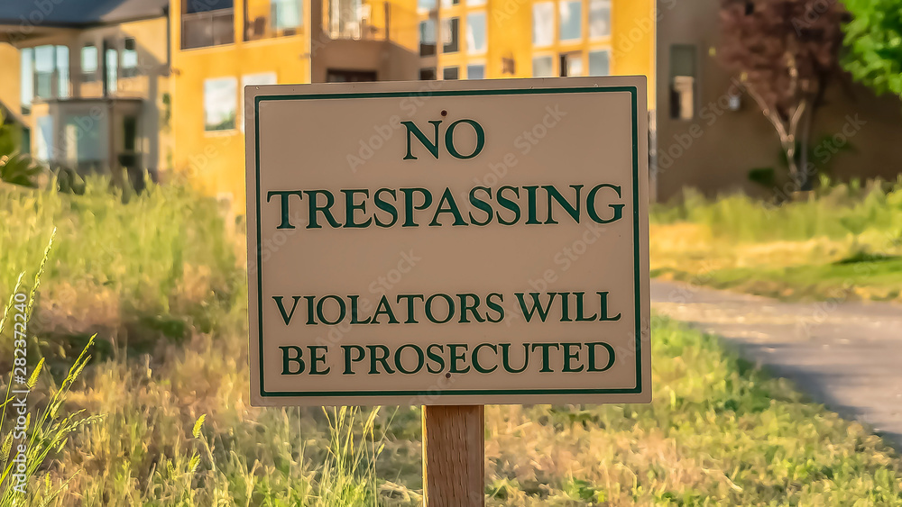 Obraz premium Panorama frame Close up of No Trespassing sign post beside a paved road that leads to houses