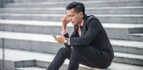Stressed and angry asian businessman looking at smartphone screen with irritation. Annoyed male received bad news, device gadget broken or dead concept