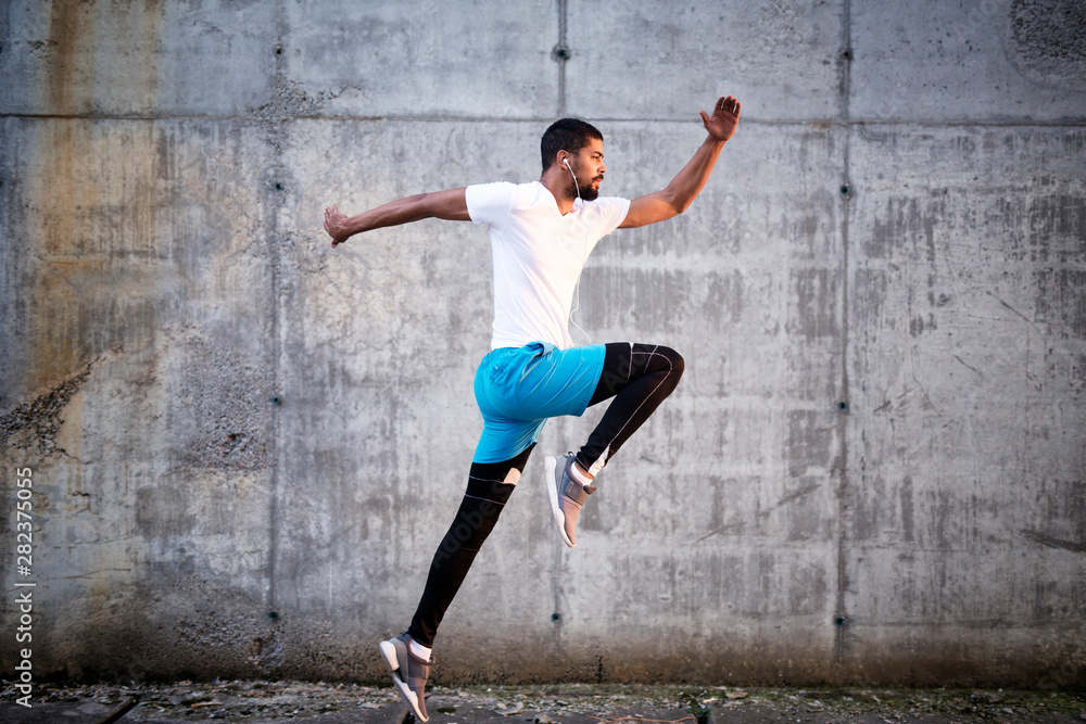 Shot of young sporty athlete jump against concrete wall background. Fitness exercise and training.