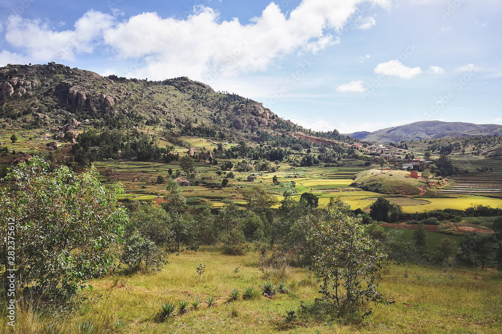 Typical Madagascar landscape in region near Tsiafahy, small hills covered with green grass and bushes, red clay houses and rice fields near.