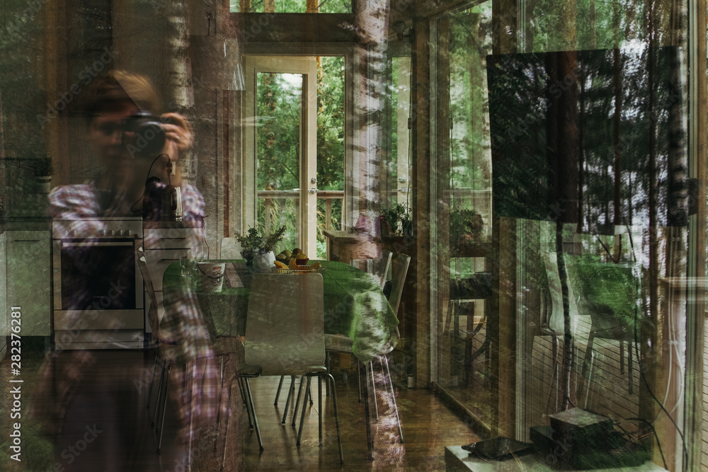Reflection of a girl photographing a room in a cabin in the woods through a window