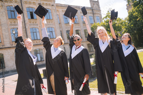 Cheerful graduates raising their masters caps in the air.