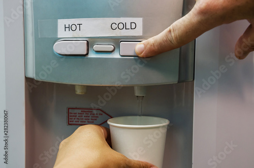 a hand with a glass pours cold water from a cooler. Close-up.