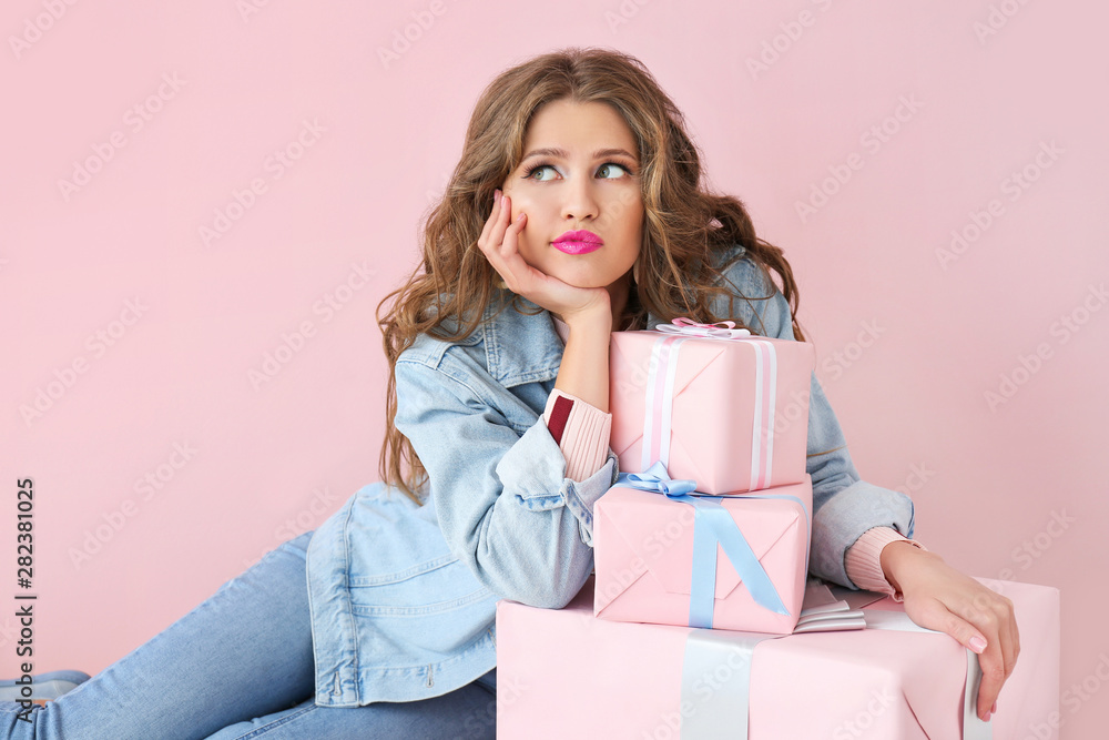 Thoughtful young woman with gift boxes on color background Thoughtful young woman with gift boxes on color background
