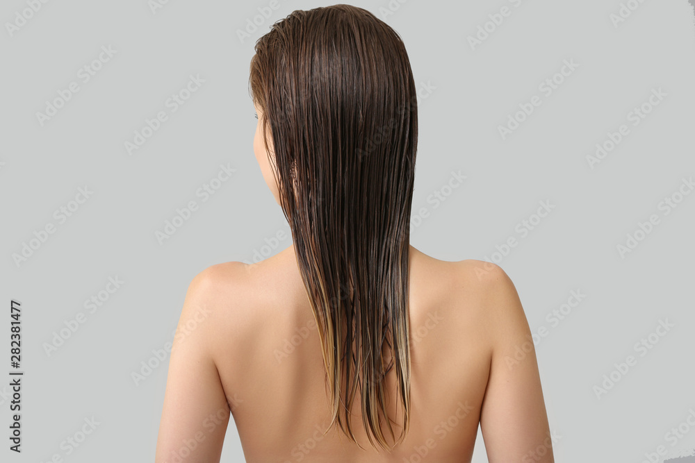 Beautiful young woman after washing hair against grey background, back view Beautiful young woman after washing hair against grey background, back view