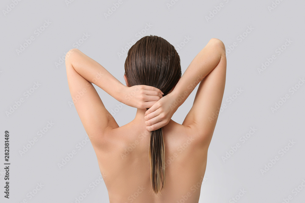 Beautiful young woman after washing hair against grey background, back view Beautiful young woman after washing hair against grey background, back view