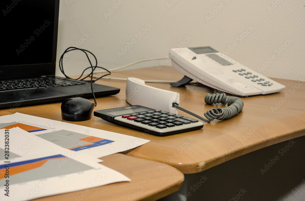 business graphs, laptop, calculator and office phone on the table. Work in process business graphs, laptop, calculator and office phone on the table. Work in process