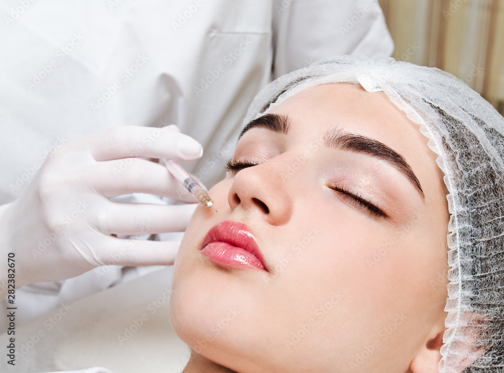 The doctor cosmetologist beautician makes the rejuvenating facial botox injections procedure for tightening and smoothing wrinkles on the face skin of a beautiful young woman in a beauty salon