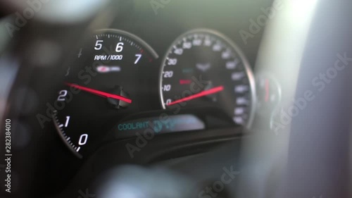 Dashboard speedometer and tachometer of a sports car shooting through the steering wheel. Close-up and selective focus of the tachometer needle