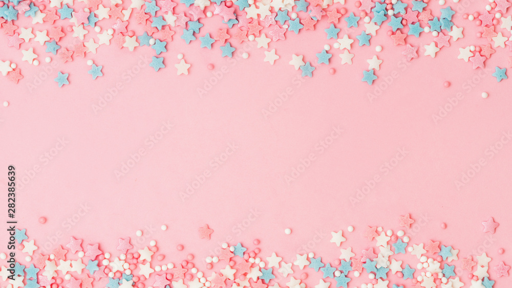 Festive border frame of colorful pastel sprinkles on pink background