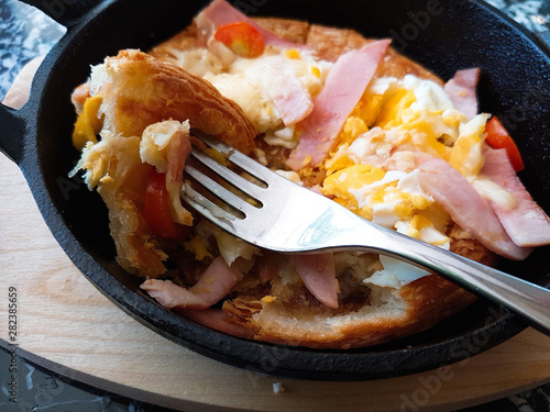 Pizza food, ham sausages, fried eggs, tomato sauce in a black pan.