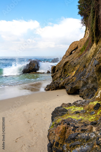 Ocean waves breaking on rocks offshore at Wood's Cove in Laguna Beach, California. Detailed closeup of colorful moss and lichens growing on rugged cliffs in the foreground.