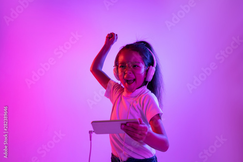 Beautiful female portrait isolated on purple backgroud in neon light. Emotional girl in eyeglasses. Human emotions, facial expression concept. Dancing, listening to music, gaming and winning.