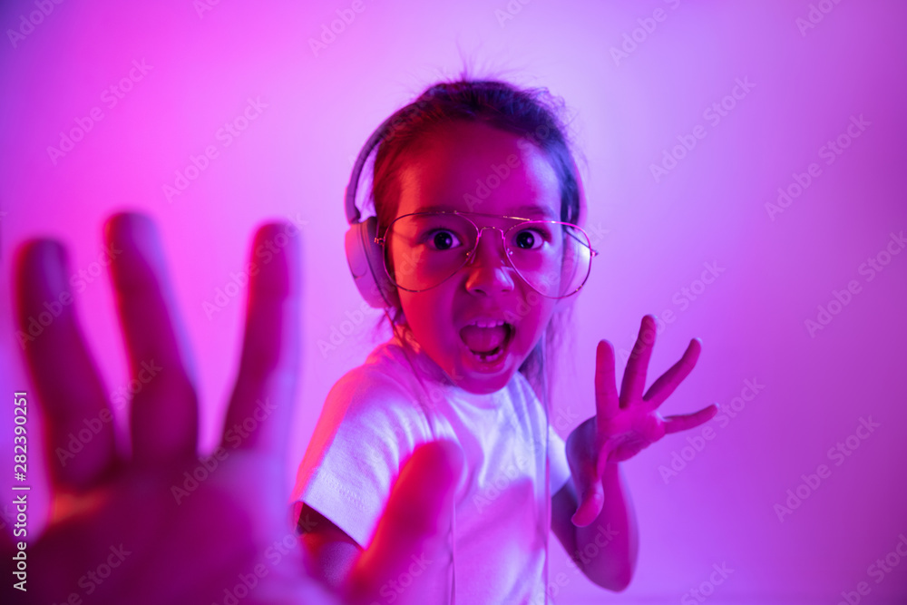 Beautiful female half-length portrait isolated on purple backgroud in neon light. Emotional girl in eyeglasses. Human emotions, facial expression concept. Dancing, listening to music, singing Beautiful female half-length portrait isolated on purple backgroud in neon light. Emotional girl in eyeglasses. Human emotions, facial expression concept. Dancing, listening to music, singing