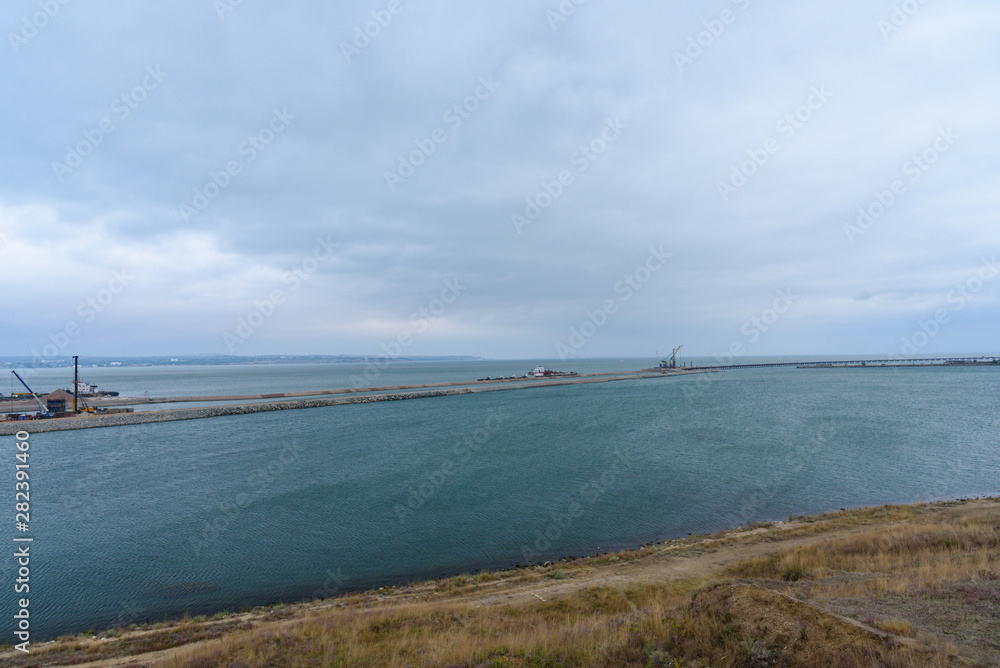 The shore of the Kerch Strait during the construction of the Kerch Bridge in cloudy weather with clouds in the sky.