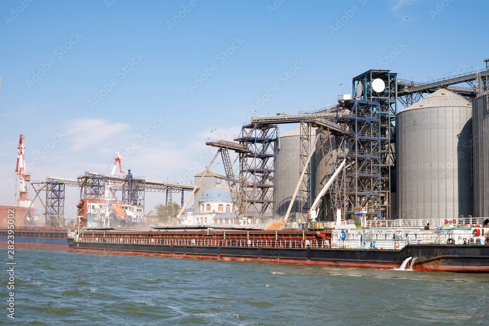 Loading grain on a ship in the port. View from the river to the port infrastructure, grain storage terminals. Transportation of grain, agribusiness.