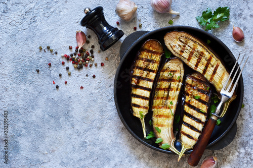 Spicy eggplant grilled in a cast-iron frying pan on a concrete background.