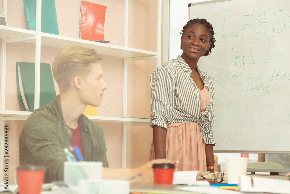 Cheerful young international teacher standing near board Cheerful young international teacher standing near board