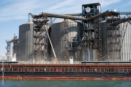 Loading grain on a ship in the port. View from the river to the port infrastructure, grain storage terminals. Transportation of grain, agribusiness.