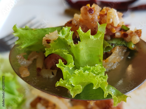 Fried Nham Salad, sour pork, Thai hot spicy food with chillis and green lettuce vegetables in a spoon.