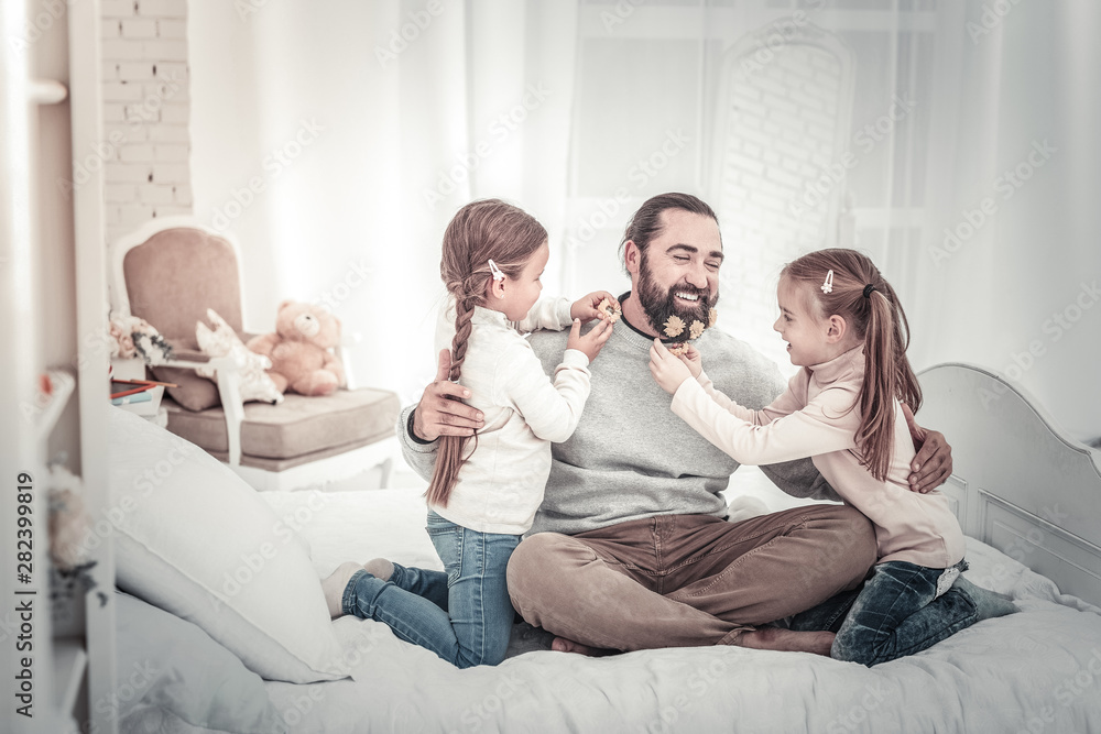 Dad and two daughters sitting on bed playing together