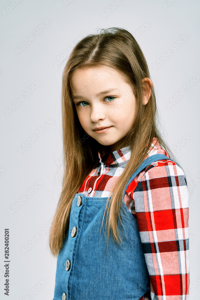 Fashionable portrait of a little girl in a denim jumpsuit and a plaid shirt. children's studio shooting. Fashionable portrait of a little girl in a denim jumpsuit and a plaid shirt. children's studio shooting.