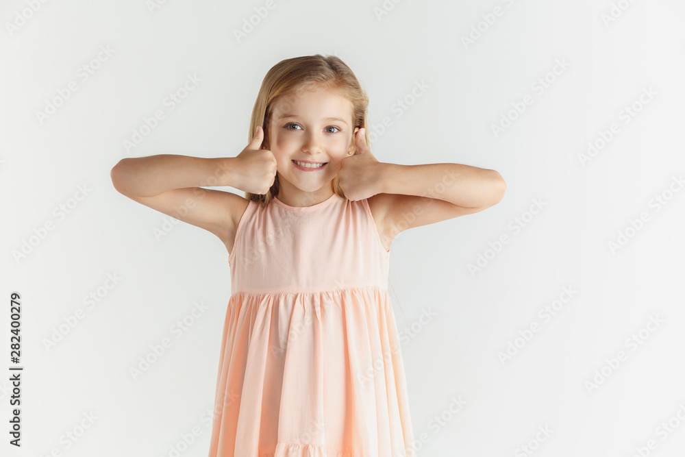 Stylish little smiling girl posing in dress isolated on white studio background. Caucasian blonde female model. Human emotions, facial expression, childhood. Looks calm, showing the sign of nice. Stylish little smiling girl posing in dress isolated on white studio background. Caucasian blonde female model. Human emotions, facial expression, childhood. Looks calm, showing the sign of nice.