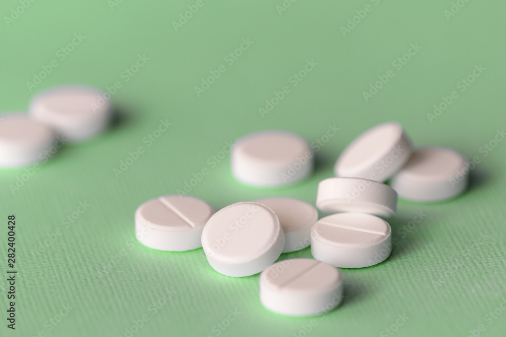 White tablets scattered on a green background close up White tablets scattered on a green background close up