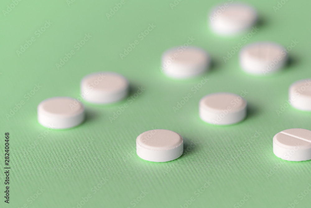 White tablets scattered on a green background close up White tablets scattered on a green background close up