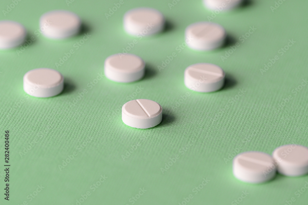 White tablets scattered on a green background close up White tablets scattered on a green background close up