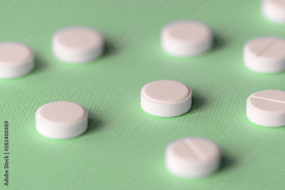 White tablets scattered on a green background close up White tablets scattered on a green background close up