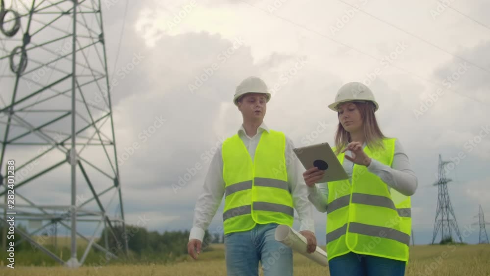 Power lines, a man and a woman engineers with a tablet in their hands discussing the progress of the construction project. Power lines, a man and a woman engineers with a tablet in their hands discussing the progress of the construction project.