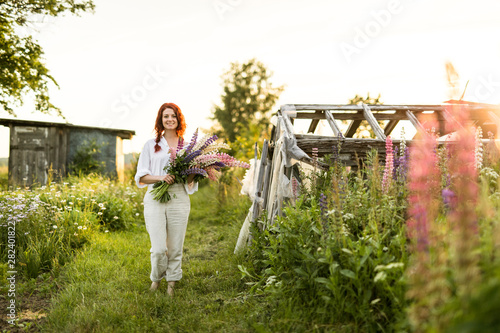 A happily smiling girl walking down the path holding lupin flowers