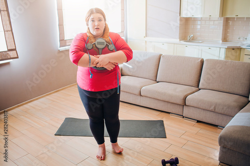 Scared confused young plus size model look on camera. Holding weight scale in hands. Stand in living room. Body positive.