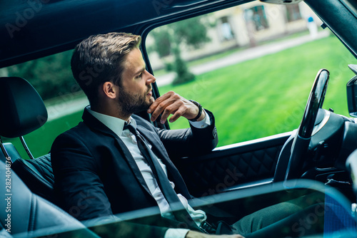 Sive view shot of mindfull handsome young man in full suit looking through the window while sitting in the car photo