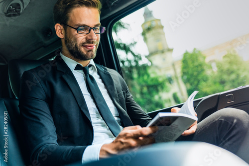 Young businessman sitting inside car and reading book © InsideCreativeHouse
