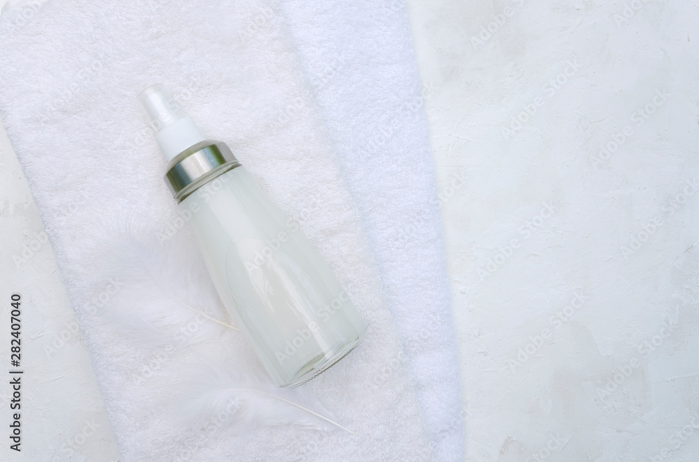 Fototapeta premium Clean white towels glass bottle of softener and feathers on it.Empty space for text
