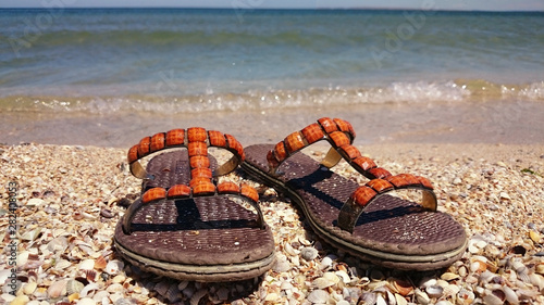 Sandals on the shell shore. In the background is the sea.