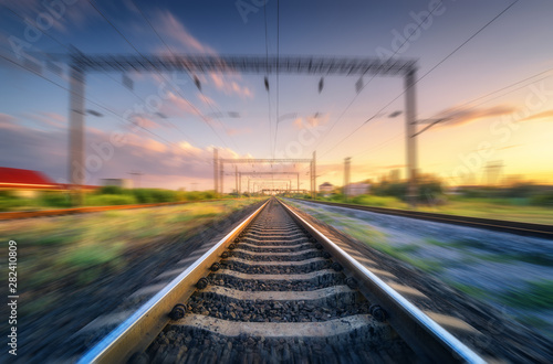 Railroad and beautiful sky at sunset with motion blur effect in summer. Industrial landscape with railway station and blurred background with colorful sky.  Railway platform in speed motion. Sleepers