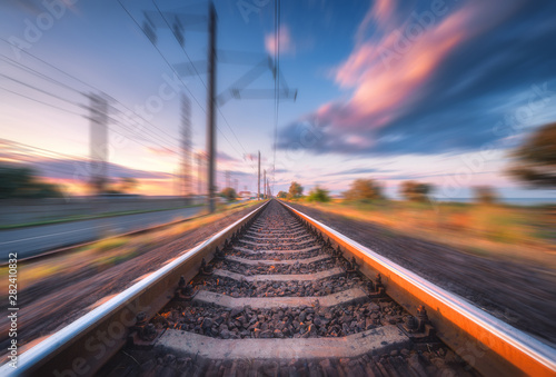 Railroad and beautiful blue sky with clouds at sunset with motion blur effect in summer. Industrial landscape with railway station and blurred background. Railway platform in speed motion. Concept