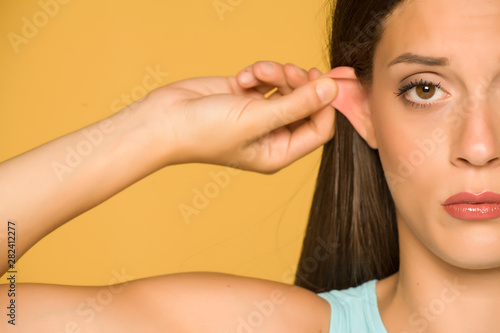 Beautiful young woman pulling her ear with her fingers on yellow background