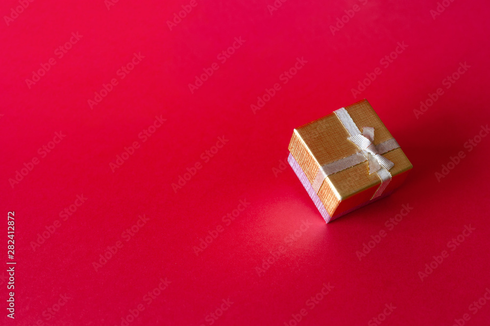 Gold gift box with a ribbon tied with a bow on a red background with a place for inscription. Gold gift box with a ribbon tied with a bow on a red background with a place for inscription.