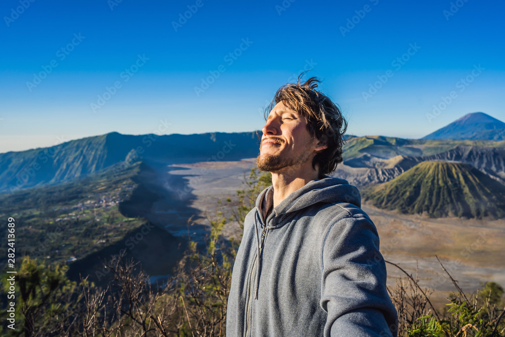 Naklejka premium Young man meets the sunrise at the Bromo Tengger Semeru National Park on the Java Island, Indonesia. He enjoys magnificent view on the Bromo or Gunung Bromo on Indonesian, Semeru and other volcanoes
