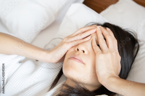 Woman stretching in bed after waking up, back view. Woman sitting near the big white window while stretching on bed after waking up with sunrise at morning, back view.