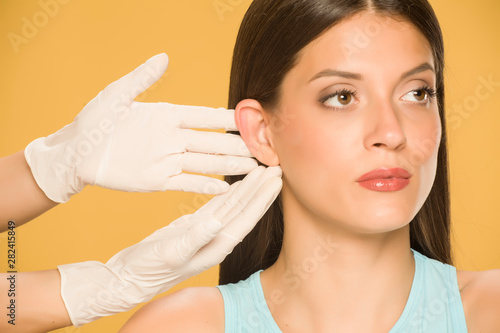 Doctor's hands touching the nose of a young woman on yellow background photo