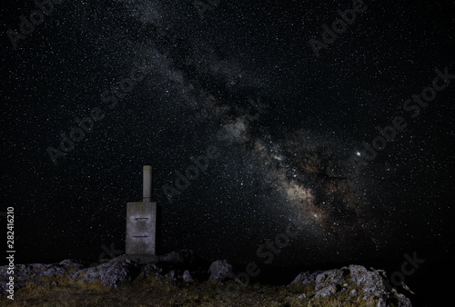 At the top of Monte Ardal mountain near the Spanish city of Yeste. It is night and the Milky Way is visible in the sky. A stone block marks the summit point.