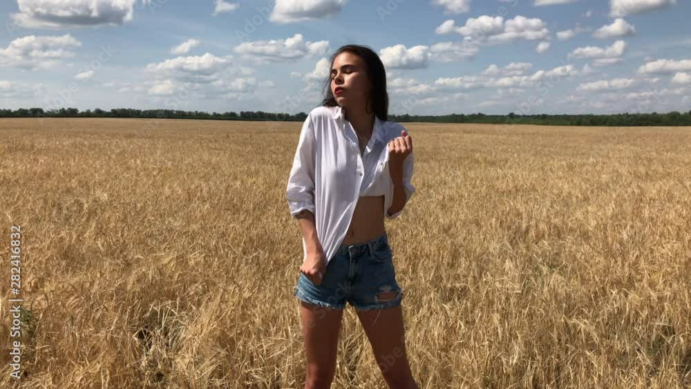 Young beautiful girl in a white shirt and blue denim shorts posing in a wheat field Young beautiful girl in a white shirt and blue denim shorts posing in a wheat field