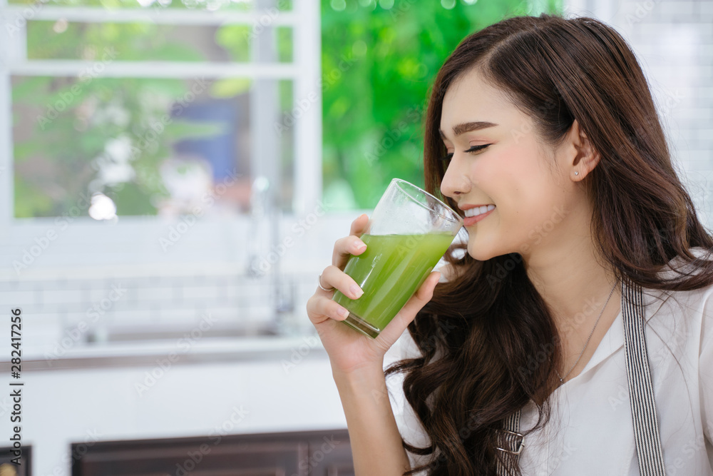 young girl drinking green cocktail with a straw.Woman drinking a homemade green detox juice. texting on her phone while sitting in her kitchen table young girl drinking green cocktail with a straw.Woman drinking a homemade green detox juice. texting on her phone while sitting in her kitchen table
