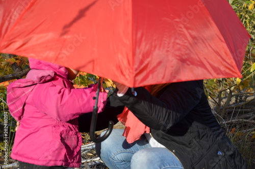 mom and daughter are walking in the autumn forest. Beautiful red, yellow leaves and red umbrella. Young mother and little toddler daughter girl in a beret and a coat walk in the autumn forest. photo