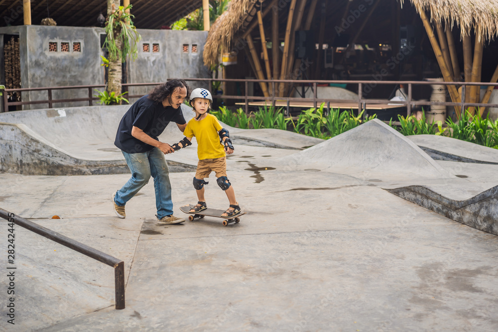 Athletic boy learns to skateboard with a trainer in a skate park. Children education, sports Athletic boy learns to skateboard with a trainer in a skate park. Children education, sports